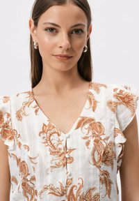 Biała bluzka z pomarańczowym wzorem paisley, krótki falbaniasty rękaw, dekolt w szpic i ozdobne guziki z przodu. Teksturowana tkanina.