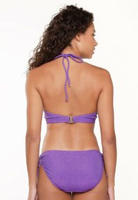 Ensemble de bikini violet avec un design à col halter, des liens ajustables et des détails froncés sur les côtés. Fabriqué dans un tissu texturé et scintillant.