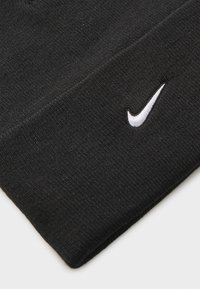 Juodas megztas kepuraitė su tekstūruotu paviršiumi ir balta siuvinėta "Nike" swoosh logo šone. Paprastas dizainas ir prigludusi forma.