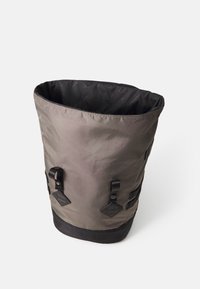 Sac seau en tissu imperméable gris avec une texture lisse, intérieur noir, et deux bandes latérales avec des accents carrés pour une fermeture sécurisée.
