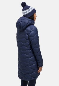 Marineblauwe gewatteerde jas met capuchon, met een golvende stikpatroon. Vergezeld van een bijpassende marineblauwe muts met een witte band en pompon.