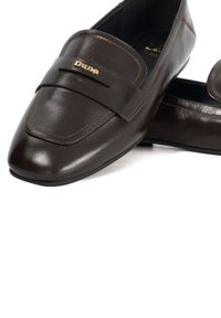 Bruine leren loafers met een gladde textuur, met een gestikt ontwerp en een gouden "Dune"-logo op een decoratieve band.