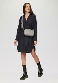 Umhängetasche aus grauem Leder. Rechteckige Form mit Reißverschluss, verstellbarem Trageriemen und runder Seitentasche. Texturierte Oberfläche, minimalistisches Design.