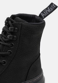 Stivale in pelle nera texture con lacci, colletto imbottito e linguetta con marca sul retro su uno sfondo bianco.