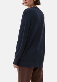 Granatowy dziergany sweter z długimi rękawami, okrągłym dekoltem i prążkowymi mankietami. Miękka faktura i luźny krój. Szwy zdobiące ramiona.