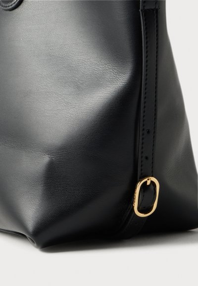Coin de sac en cuir noir avec une boucle dorée brillante sur une sangle réglable, montrant la texture et les détails de couture.