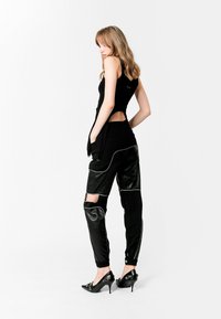 Top negro sin mangas con cortes, emparejado con pantalones cargo negros con detalles de cuero y cortes en las rodillas, y zapatos de tacón alto negros y brillantes.