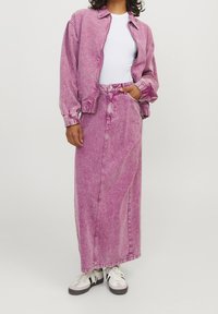 Rosa denimjacka och matchande lång kjol med rak skärning och fickor. Vit t-shirt under och avslappnade sneakers fulländar outfiten.