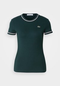 Tamnozelena majica kratkih rukava, prilagođenog kroja, s bijelim obrubom na ovratniku i rukavima, s malim Lacoste logotipom na prsima.