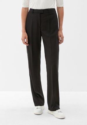 Pantalons noirs ajustés avec une texture lisse, design à jambe droite, passants de ceinture et pli avant. Portés avec des baskets blanches.