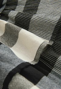 Tissu à carreaux en noir, blanc et gris, présentant divers motifs avec une texture tissée et des designs rayés contrastés.