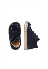 Scarpe suede blu navy con suola in gomma beige, punta arrotondata, cuciture bianche e design con lacci blu. La vista laterale mostra un leggero tacco.