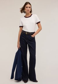 Untricou alb cu margine ondulată de culoare vișinie, purtat cu blugi evazați de culoare albastru închis și un sacou bleumarin, accessorii cu cercei rotunzi din aur.