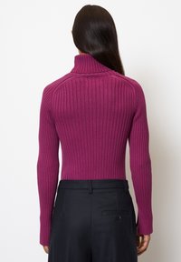 Fitted turtleneck sweater in vibrant magenta, featuring ribbed texture and long sleeves. Paired with tailored black pants.