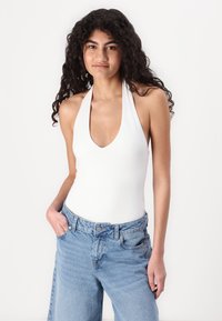 Balta halter-neck bodijs ar dziļu V veida kakla izgriezumu, kopā ar gaismas zila plaša piegriezuma denimām biksēm, kas ir augstā jostasvietā un ar sānu kabatām.