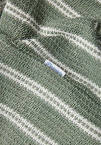 Tissu tricoté à rayures vertes et blanches avec une texture douce. Présente une petite étiquette "Premium" en bleu.