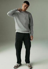 Grauer Baumwoll-Sweatshirt mit langen Ärmeln, kombiniert mit schwarzen Cargo-Hosen mit Seitentaschen und grauen Sneakers mit weißen Akzenten.