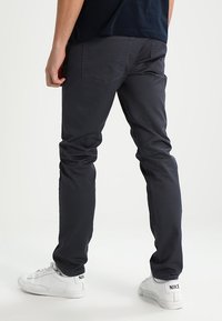 Mørkegrå slim-fit bukser med en glat tekstur, der har baglommer og er parret med hvide sneakers.