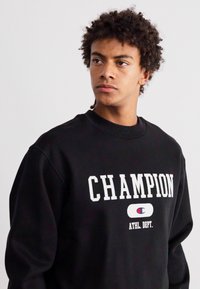 Hanorac negru cu text și logo alb "CHAMPION". Gât rotund, mâneci lungi cu manșete ribbate. Țesătură moale, texturată.