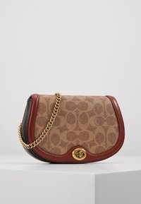 Sac bandoulière en toile beige avec des accents en cuir marron, bandoulière chaîne dorée et motif de logo embossé sur le devant. Forme arrondie et fermeture à bascule.