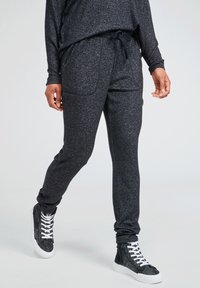 Black jogger pants with a heathered texture, elastic waistband, drawstring, and side pockets, paired with high-top sneakers.