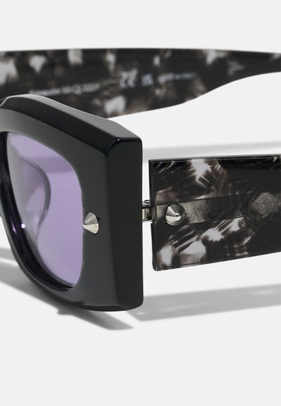 Occhiali da sole oversize neri con lenti viola; la montatura strutturata presenta una texture grigia e nera sul tempio, accentuata da dettagli in argento.