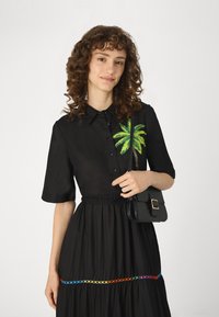 Rochie neagră cu mâneci scurte, având un design cu frunze de palmier verzi pe partea stângă și accente brodate multicolore pe margine.