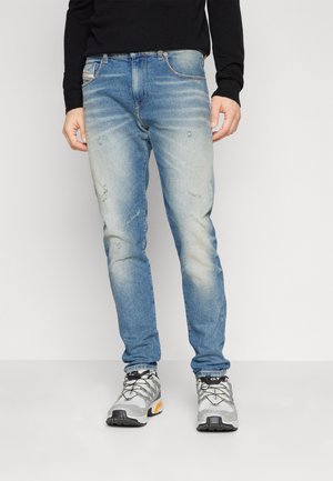 Light blue denim jeans with faded areas and distressed detailing. Worn with gray and orange athletic shoes. Straight leg fit.