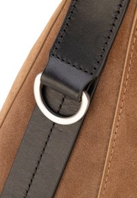 Correa de bolso de ante marrón con detalles en cuero negro, que presenta un anillo metálico plateado y costuras detalladas, mostrando una textura suave y artesanía.