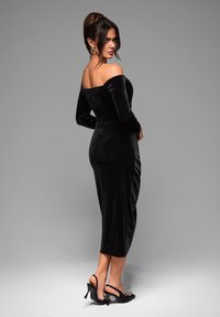 Svart sammetsklänning med axelbandslös design, långa ärmar, figursydd överdel och längd till mitten av vaden. Kombinerad med svarta slingback-klackar med dekorativ detalj.