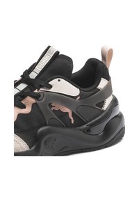 Baskets Puma noires et beiges avec un design en mesh texturé, une semelle épaisse, une languette au talon et le logo Puma sur le côté et la languette.