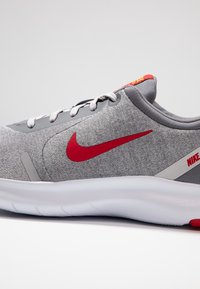 Baskets Nike grises avec logo swoosh rouge, lacets blancs, col rembourré et semelle blanche épaisse, inclinées sur un fond uni.