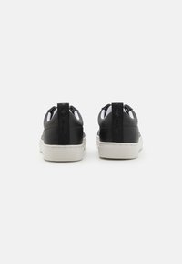 Baskets en cuir noir avec une semelle en caoutchouc blanc, des languettes et un logo au dos. Texture lisse avec de petites coutures.