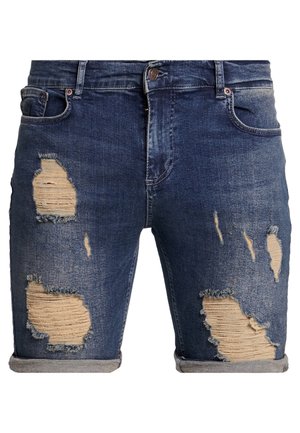 Mørkeblå denimshorts med opviklede kanter og store slidte pletter, der afslører beige stof under.