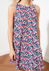 Blommig ärmlös klänning med en marinblå bakgrund och rosa och vita blommor. A-linjeform, lättviktig stoff och rund halsringning.