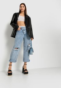 Blazer de cuero sintético negro, top corto de encaje blanco, jeans de tiro alto desgastados de color azul claro, sandalias de plataforma negras con tiras, bolso azul.