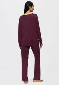 Top de manga larga, ajuste relajado y pantalones sueltos en un tejido burdeos profundo. Textura suave, detalles de costura mínimos y escote ancho.