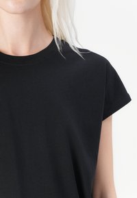 Svart t-skjorte med korte ermer og rund hals. Laget av et glatt stoff med en avslappet passform, med rene kanter og uten synlige logoer.