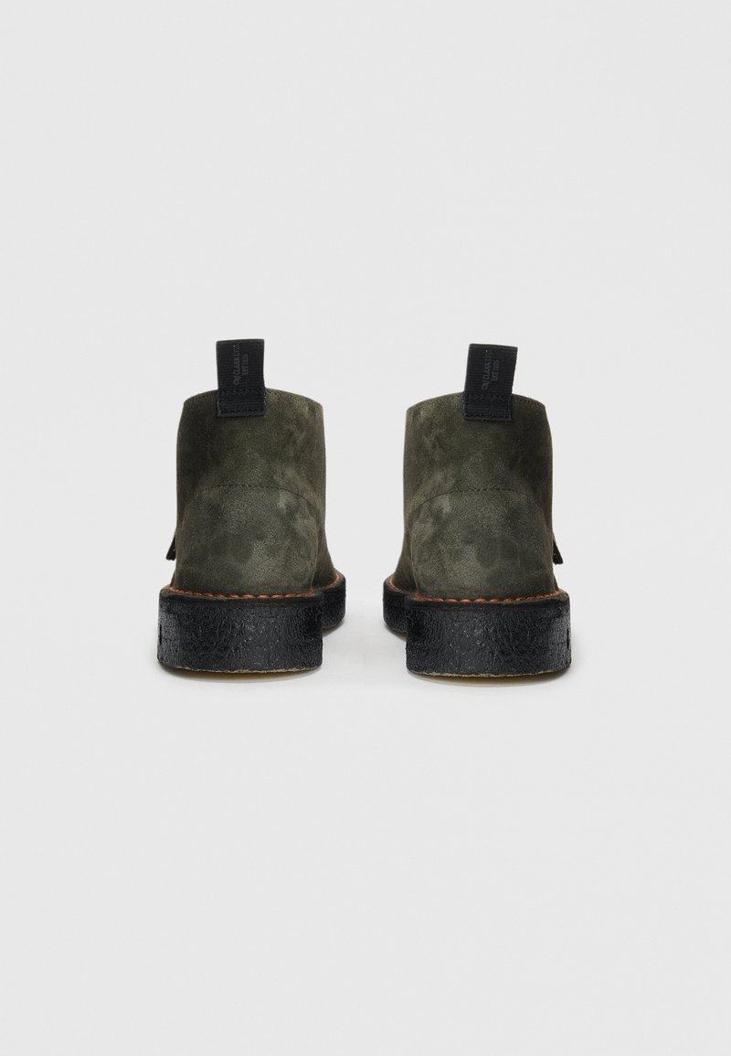 Pair of dark olive suede ankle boots with black soles and black fabric pull tabs, viewed from the back on a white background.