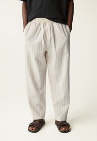 Pantalones en mezcla de lino color blanco roto con sutiles rayas verticales azules, que cuentan con una cintura elástica con cordón y un diseño de pierna ajustada.