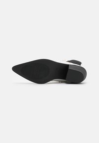 Suela de goma negra con forma de punta afilada, que presenta surcos horizontales para agarre y una sección superior lisa y contrastante.