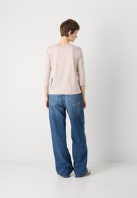 Lichtroze top met driekwartmouwen, gecombineerd met relaxed-fit, donkerblauwe denim jeans. Glad oppervlak, eenvoudig ontwerp, geen zichtbare patronen.
