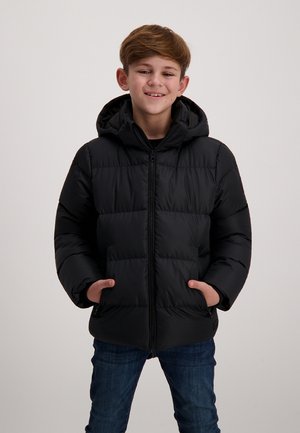 Zwarte pufferjack met een capuchon, met een ritssluiting aan de voorkant, twee voorkruimelpockets en een gewatteerd ontwerp. Draagt over een zwart shirt en blauwe jeans.