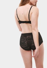 Set di lingerie in pizzo nero composto da un bralette con spalline regolabili e chiusura a gancio, abbinato a culotte in pizzo a vita alta con bordi ondulati.