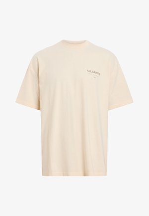 Camiseta de algodón crema con un ajuste relajado, con mangas cortas y un pequeño logo impreso en el lado izquierdo del pecho. Textura suave, diseño minimalista.