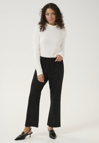 Pantalones anchos negros de textura suave y cintura elástica, combinados con una blusa ajustada de manga larga blanca. Zapatos negros de punta.