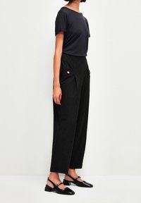 Housut, mustat, leveät lahkeet, etupuolella laskoksia ja sivutaskuja. Yhdistettynä muotoilevaan, lyhythihaiseen, tummanharmaaseen t-paitaan ja mustiin kertaa kengillä.