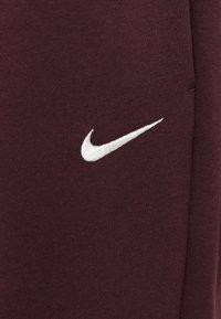 Witte geborduurde Nike swoosh logo op donker bordeaux gekleurd stof, close-up.