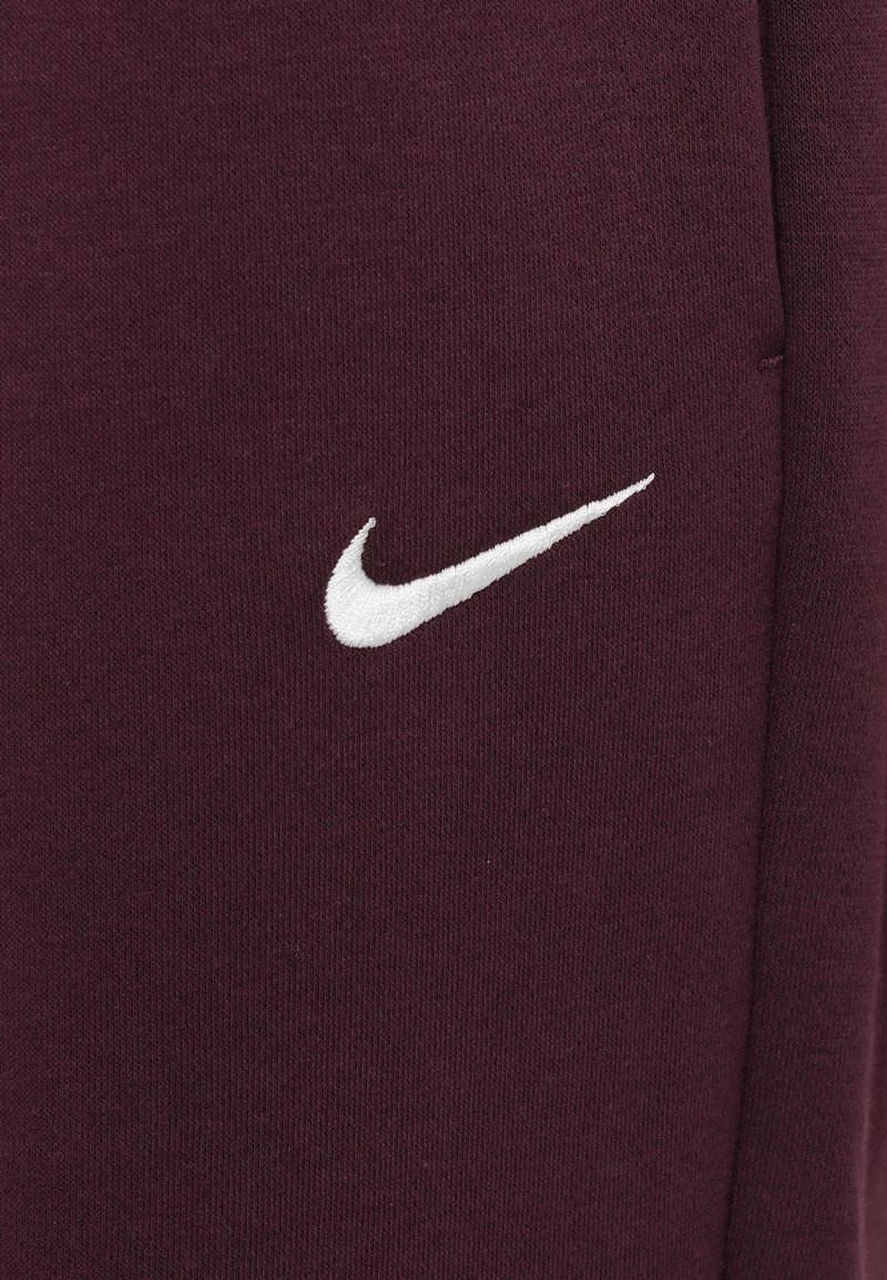 Dettaglio ravvicinato del logo Swoosh Nike ricamato in bianco su un tessuto color maroon scuro.