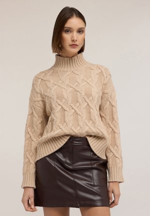 Pull en maille beige à col montant, avec un ourlet côtelé. Assorti à une jupe moulante en cuir synthétique marron avec des poches latérales.